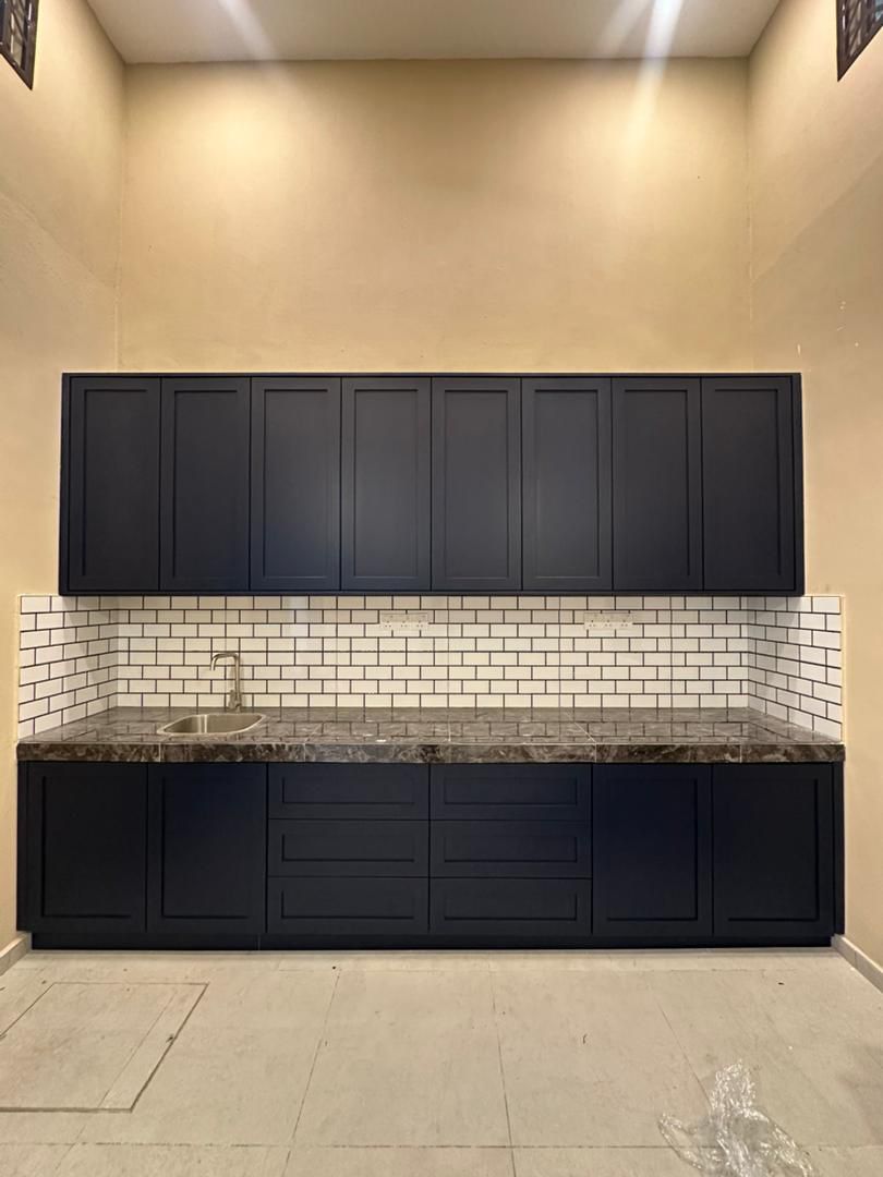 Straight run of dark upper and lower kitchen cabinets, white tiled splashback and sink